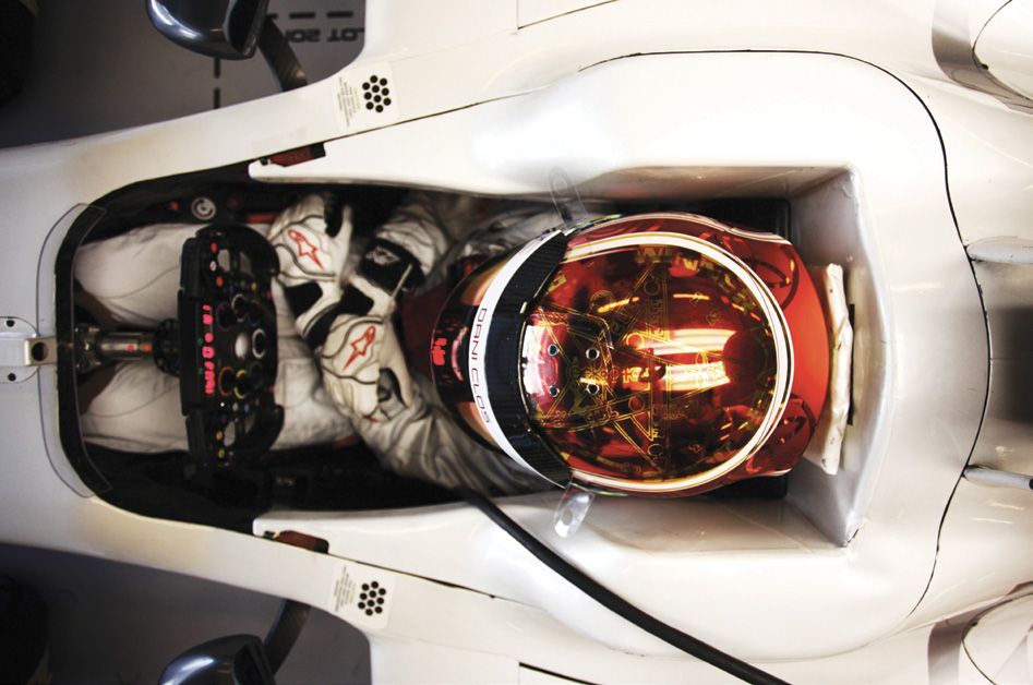 Looking down into an HRT Formula 1 cockpit: the driver in a red and white helmet.