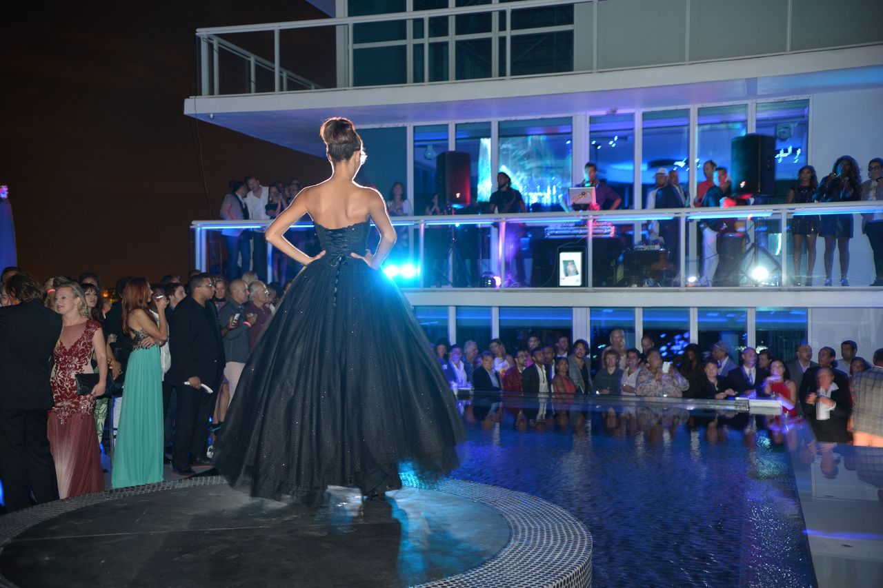 A model in a black ball gown on a round stage above the pool at the fashion show of the Le CITY deluxe Miami Anniversary Event.